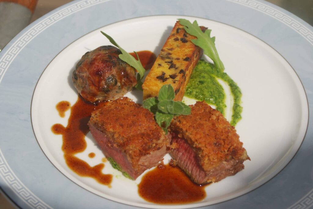 Selle d’agneau en croute de moutarde, caillette aux herbes, panisse aux olives, pesto de roquette, jus à la Nepita