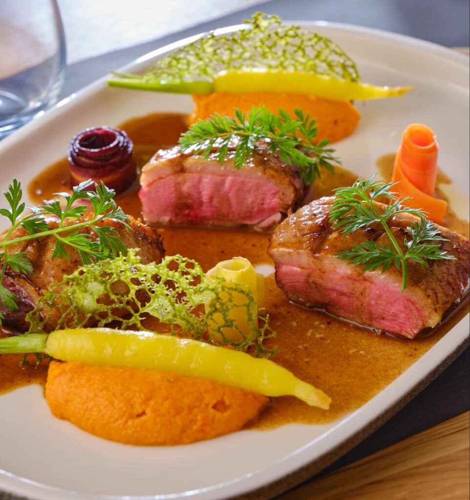 Filet de canard rôti au sang, jus de canard à l’ail noir et mousseline des sables, carottes glacées et tuile de fanes